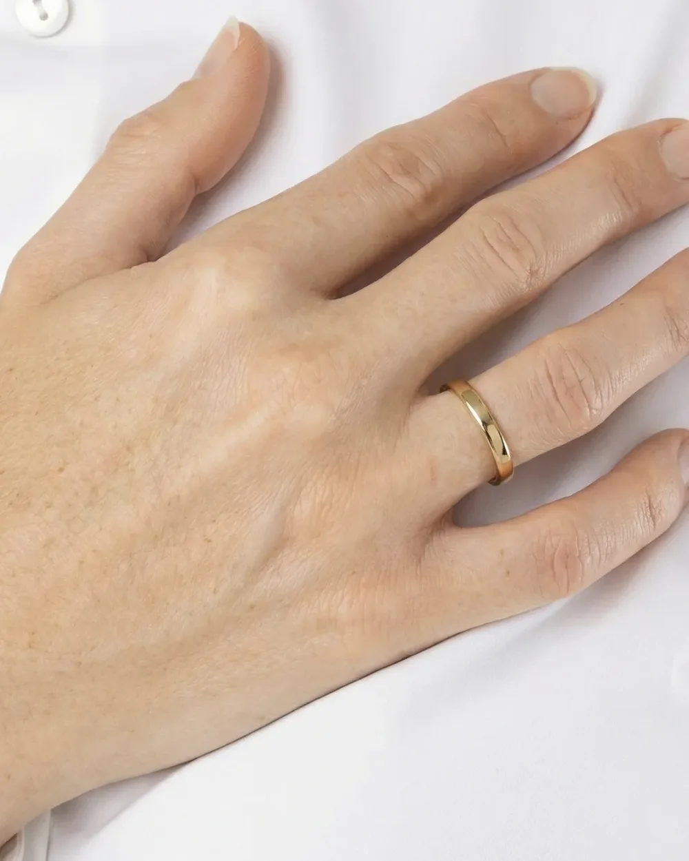 Une fine bague en or massif portée à la main, sur un chemisier blanc